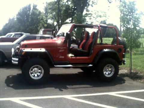 1996 Ford Bronco - A red Jeep Wrangler is parked next to other vehicles under a cloudy sky.