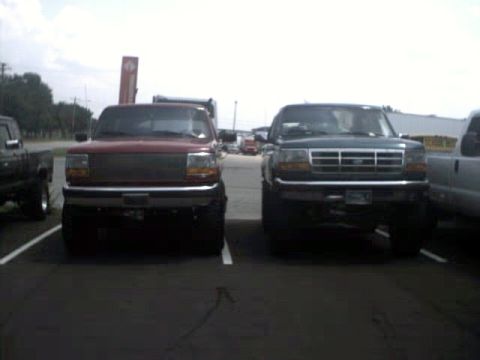 1996 Ford Bronco - Two pickup trucks are parked next to each other in a parking lot.