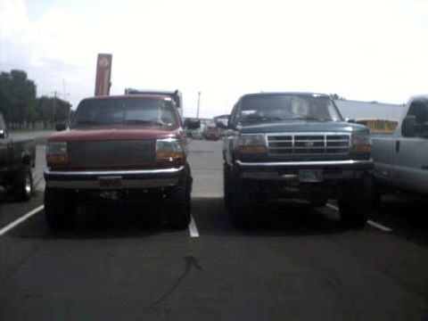 1996 Ford Bronco - Two trucks are parked in a lot under a cloudy sky. The red truck is on the left and the green truck is on the right.