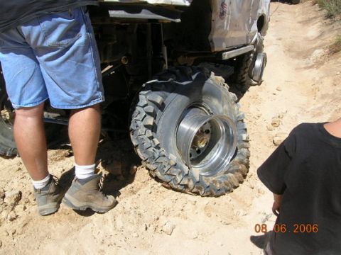 1995 Ford Bronco - A flat tire on an off-road vehicle is visible on a dirt path.