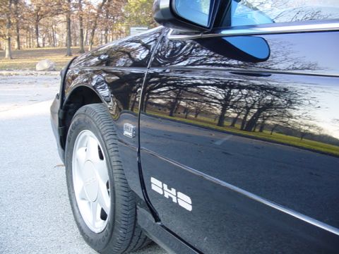 1998 Ford Taurus - The side of a black Ford Taurus SHO is shown, reflecting trees and a road.