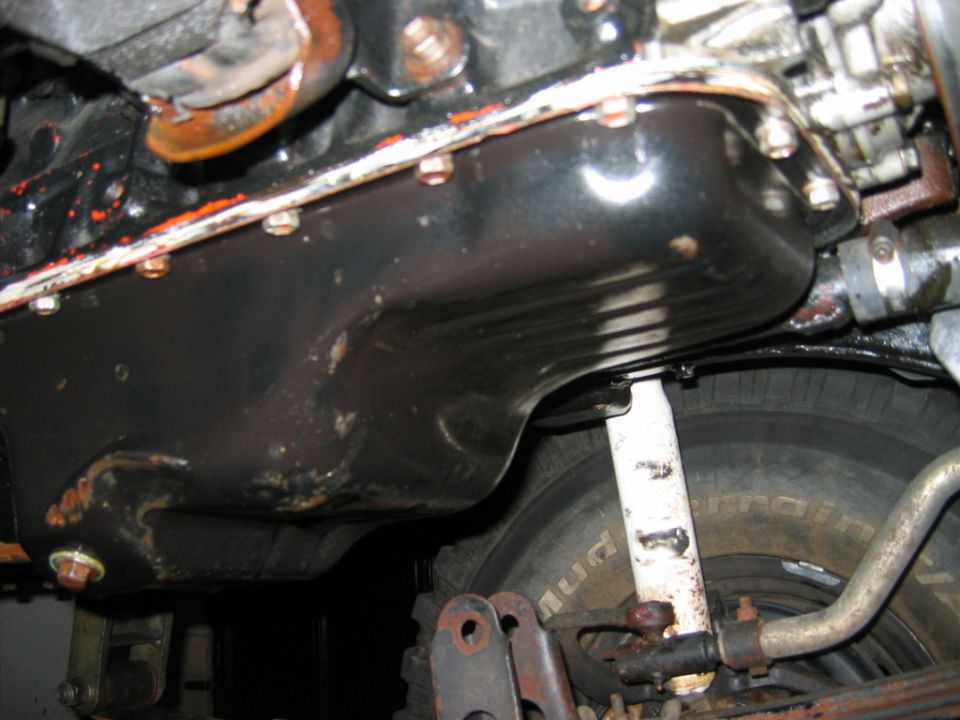 Undercarriage view of black oil pan, white shock, and tire on a vehicle