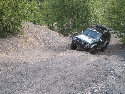 1992 Ford Bronco - A modified Jeep Cherokee XJ navigates a challenging off-road trail with steep inclines and loose gravel.