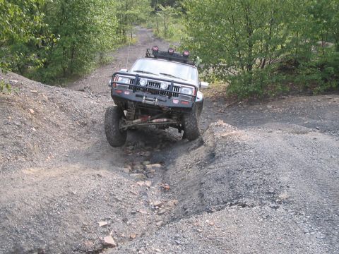 1992 Ford Bronco - An off-road vehicle tackles a challenging rocky terrain on a dirt path surrounded by trees.
