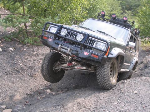 1992 Ford Bronco - Modified Jeep Cherokee navigates a challenging off-road trail with one wheel lifted.