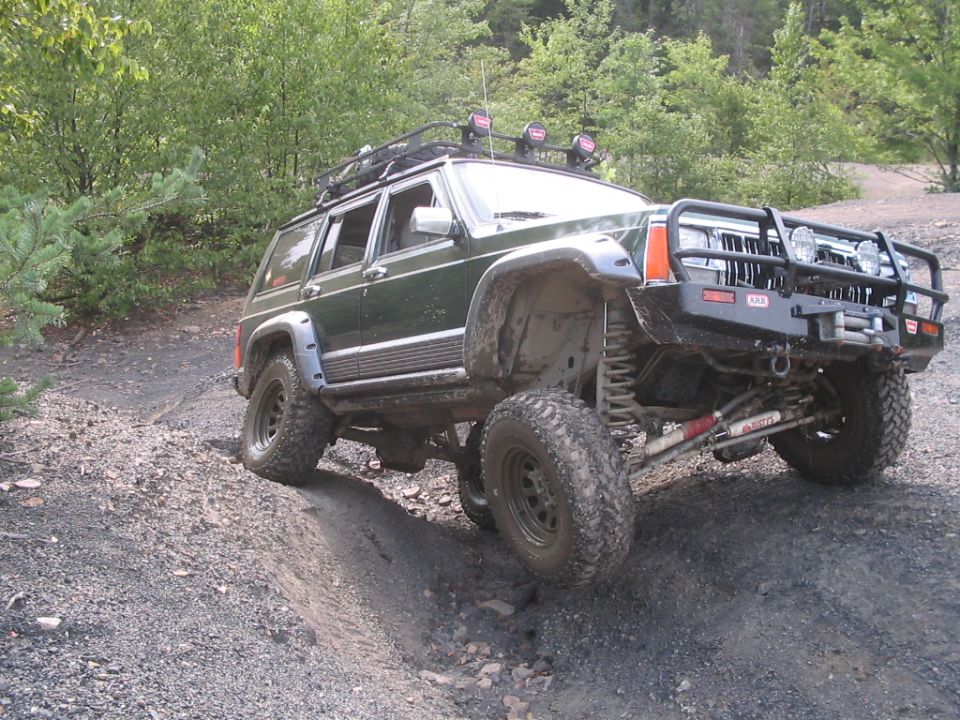 Lifted green Jeep Cherokee XJ with ARB winch bumper flexing on a rocky trail