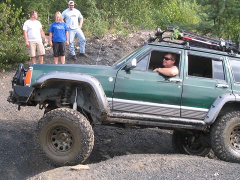 1992 Ford Bronco - A green Jeep Cherokee XJ is shown off-roading with a driver and passengers observing.