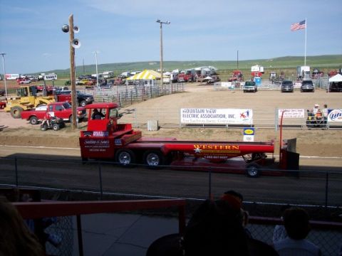 1972 Ford Ranchero - A red truck and trailer is parked at an outdoor event with an American flag flying overhead.