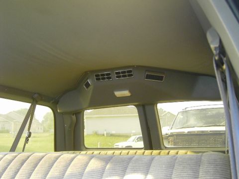 1990 Chevrolet Suburban - View from inside a vehicle's rear seat, looking out the window at another SUV and a suburban neighborhood.