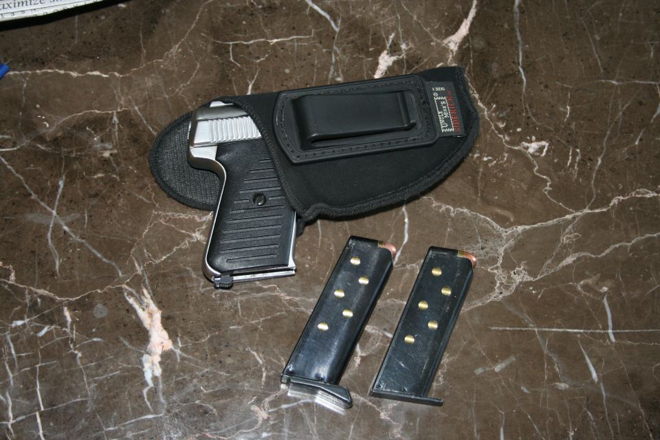 Black pistol in a holster with two loaded magazines on a marble surface