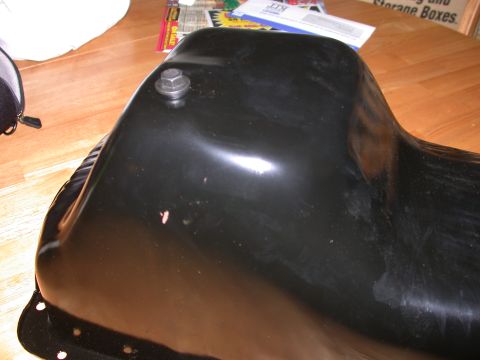 1995 Ford Bronco - A black oil pan is shown from an angled perspective, with a bolt visible on its surface.