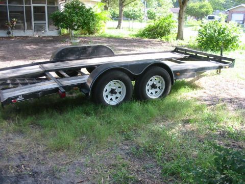 1997 Ford Crown Victoria - A dual-axle car hauler trailer sits on grassy ground near a building.