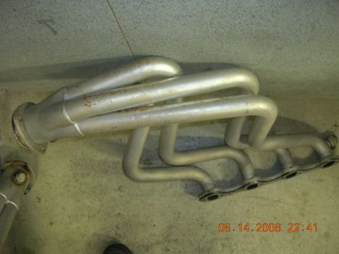 1996 Ford Bronco - A silver exhaust manifold with four pipes on each side sits on a concrete floor.