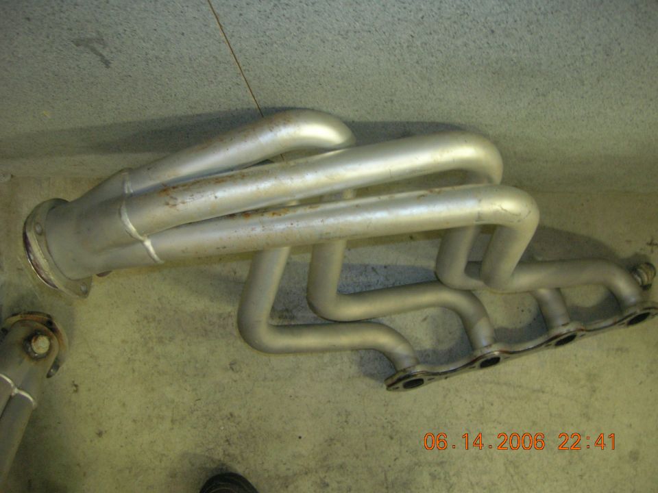 Exhaust manifold with four pipes on the left and four on the right, silver metal with rust spots