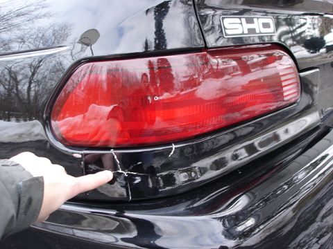 1998 Ford Taurus - Damage to the rear bumper of a car, with an SHO badge visible.