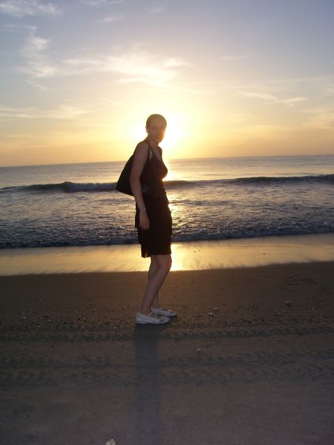 1994 Ford Probe - A woman poses on the beach as the sun sets over the ocean, with a website logo visible in the lower right corner.