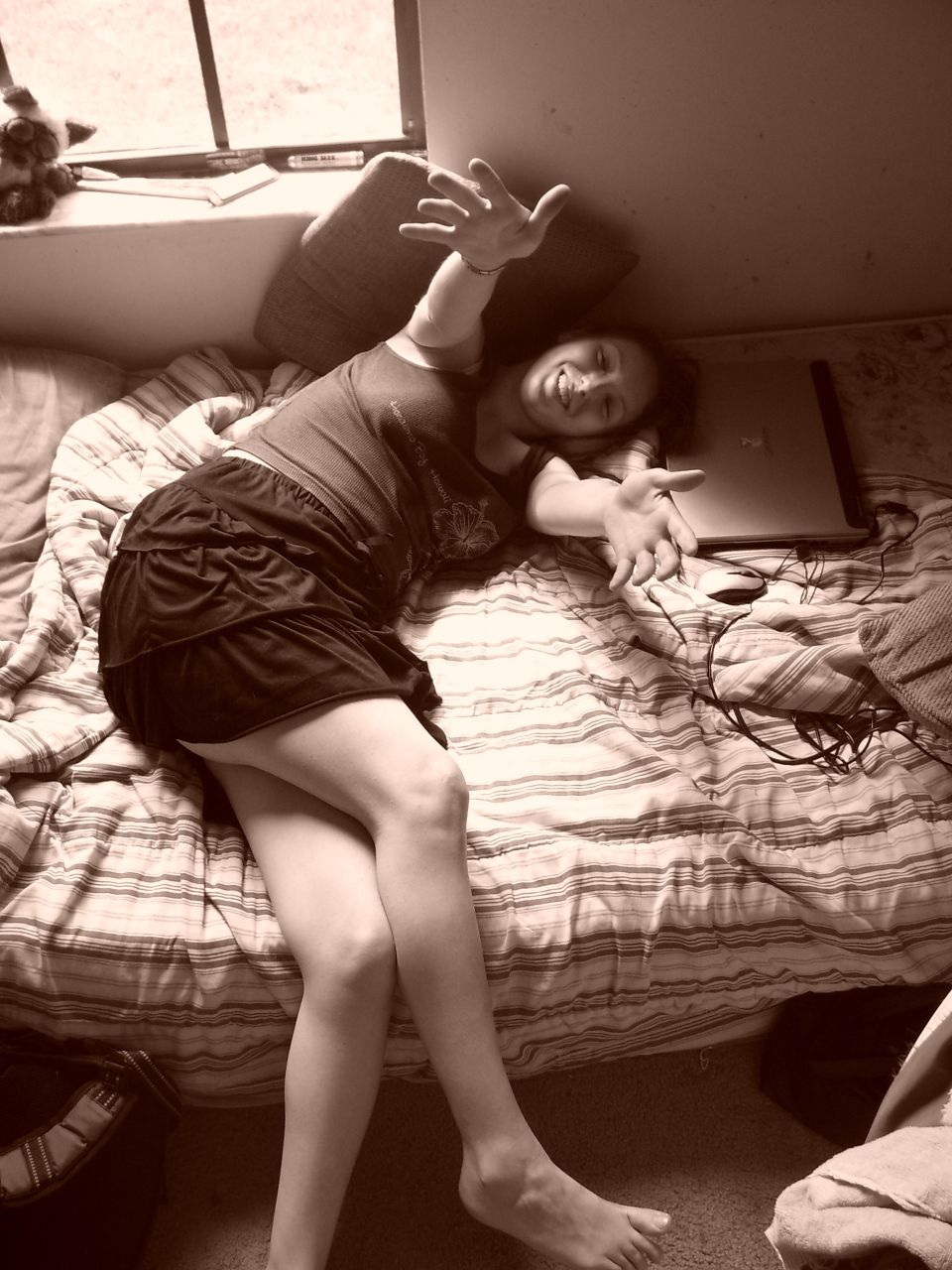 Person lying on a bed with arms outstretched, laptop nearby