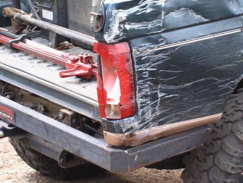 1981 Ford Bronco - This heavily damaged dark green SUV shows significant body damage and a broken taillight, with a Hi-Lift jack visible in the cargo area.