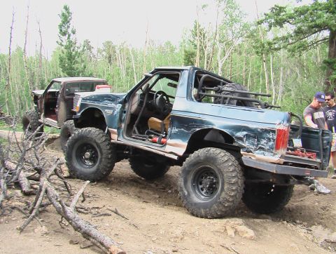 1981 Ford Bronco - Two heavily modified off-road vehicles, a 1981 Ford Bronco and a pickup truck, are parked on a dirt trail.