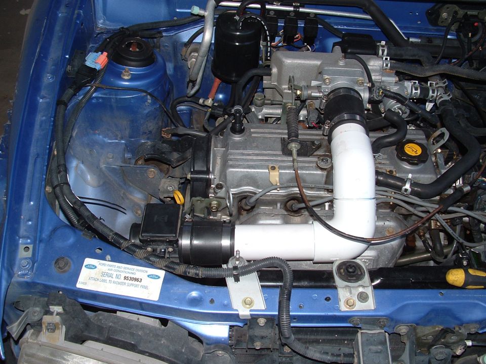 Blue car engine bay with a DIY white PVC intake pipe routed to the air meter