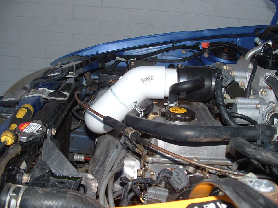 Engine bay with a DIY white PVC intake pipe clamped to the intake boot on a blue car