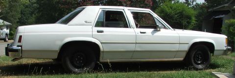 1985 Ford Crown Victoria LTD - A white sedan with a vinyl roof and tan trim is parked on a grassy area.