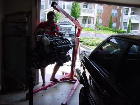 1984 BMW 3 Series - Engine hoist lifting an engine inside a garage with a car nearby.