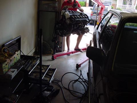 1984 BMW 3 Series - An engine is being removed from a vehicle using an engine hoist in a garage setting.