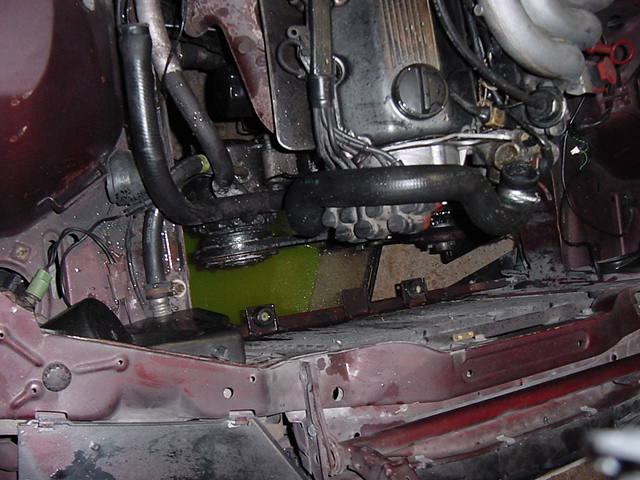 Engine bay showing a pool of green coolant and hoses connected to the engine block