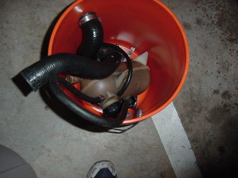 1984 BMW 3 Series - A collection of automotive hoses and a coolant reservoir are placed inside an orange bucket on a concrete floor.