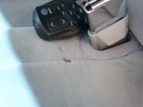 1995 Ford Crown Victoria - Detached steering-wheel-mounted audio remote control with arrow buttons lying on a gray cloth seat beside a seatbelt buckle.