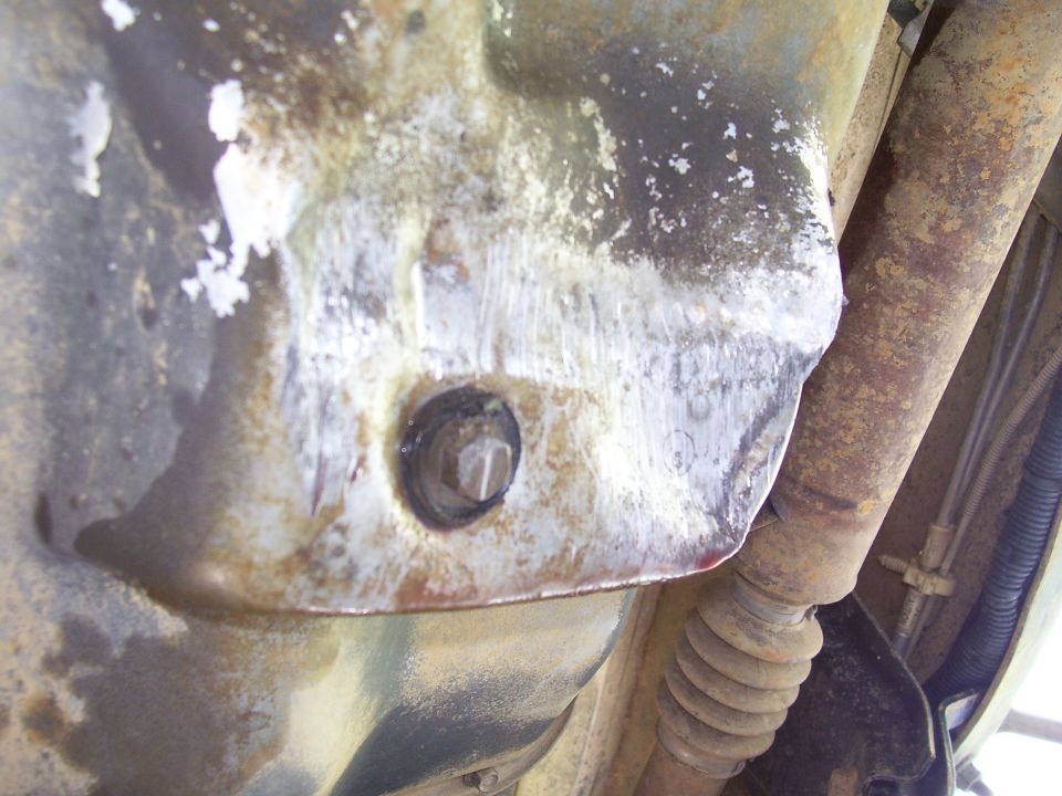 Underside of vehicle showing oil pan with drain plug and part of driveshaft