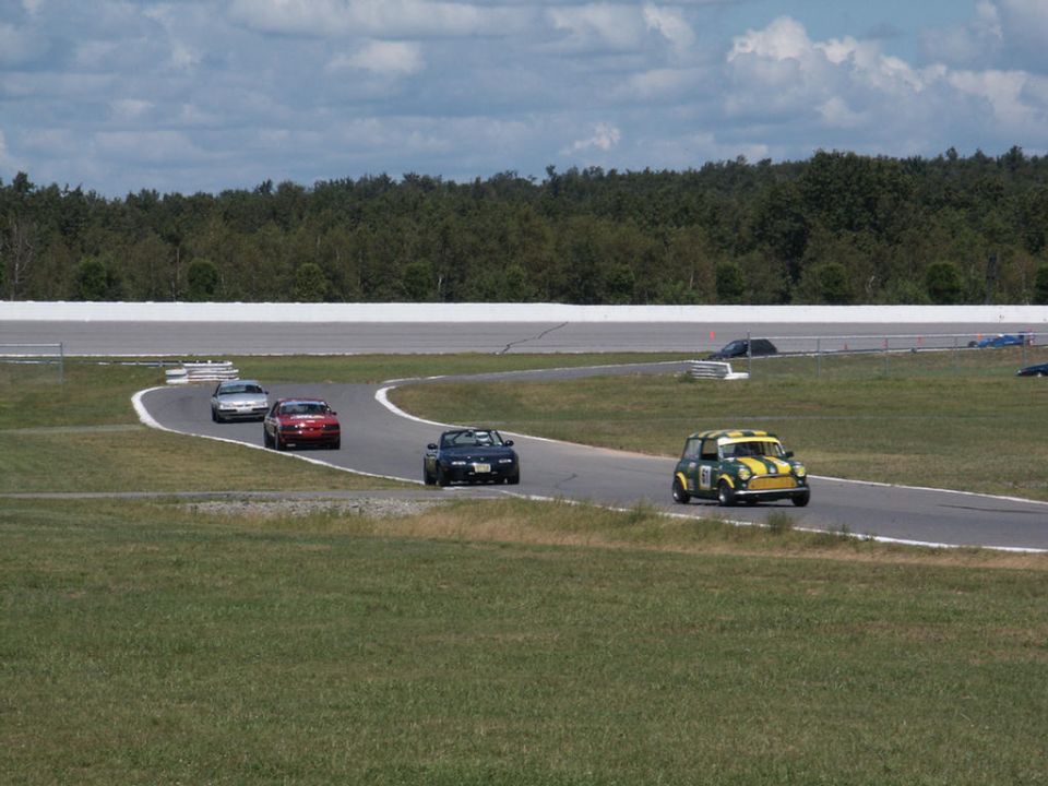 Several cars race on a track, including a yellow and green Mini Cooper