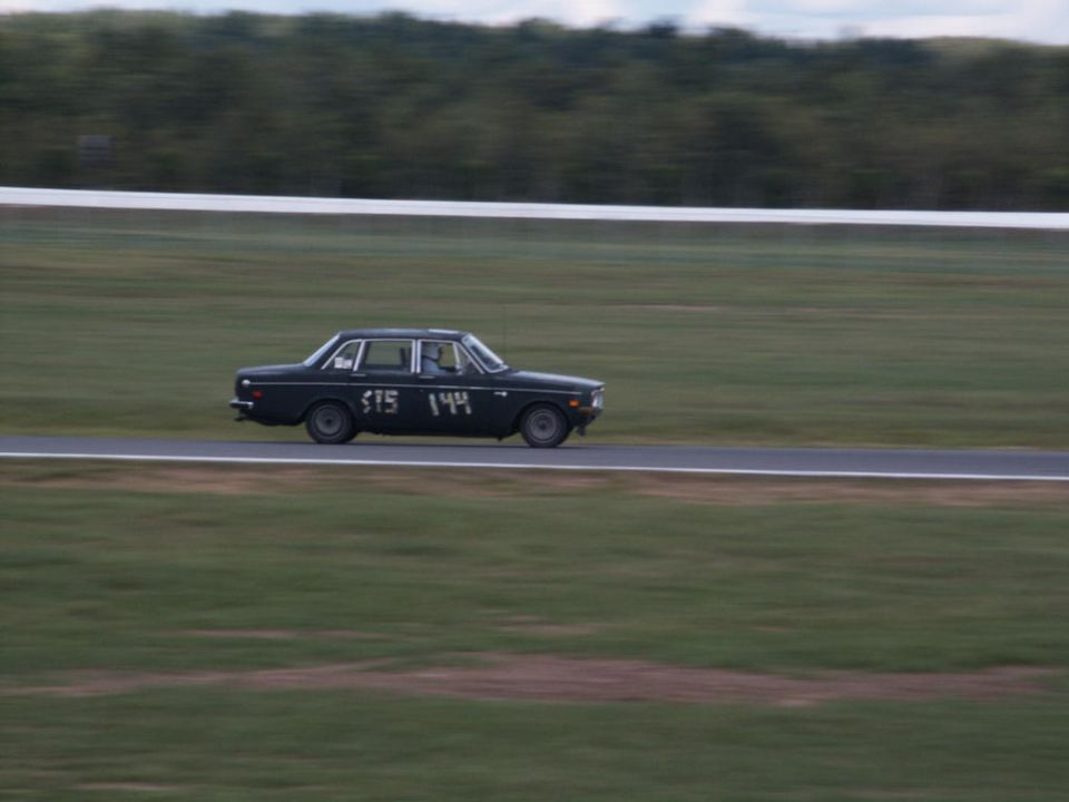 Black sedan with racing numbers 515 144 on the side, seen from the side on a race track