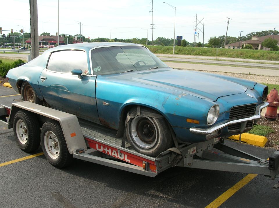 Faded blue 1970 Chevrolet Camaro project car strapped to a U-Haul trailer in a parking lot