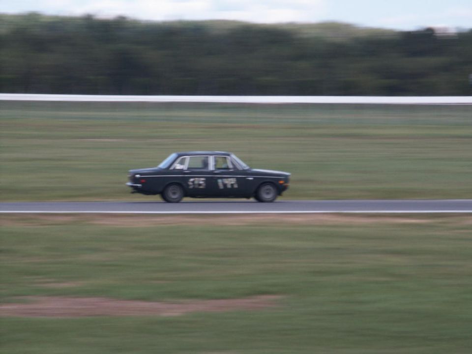 Dark sedan with racing numbers '575 194' on its side, driving on a race track