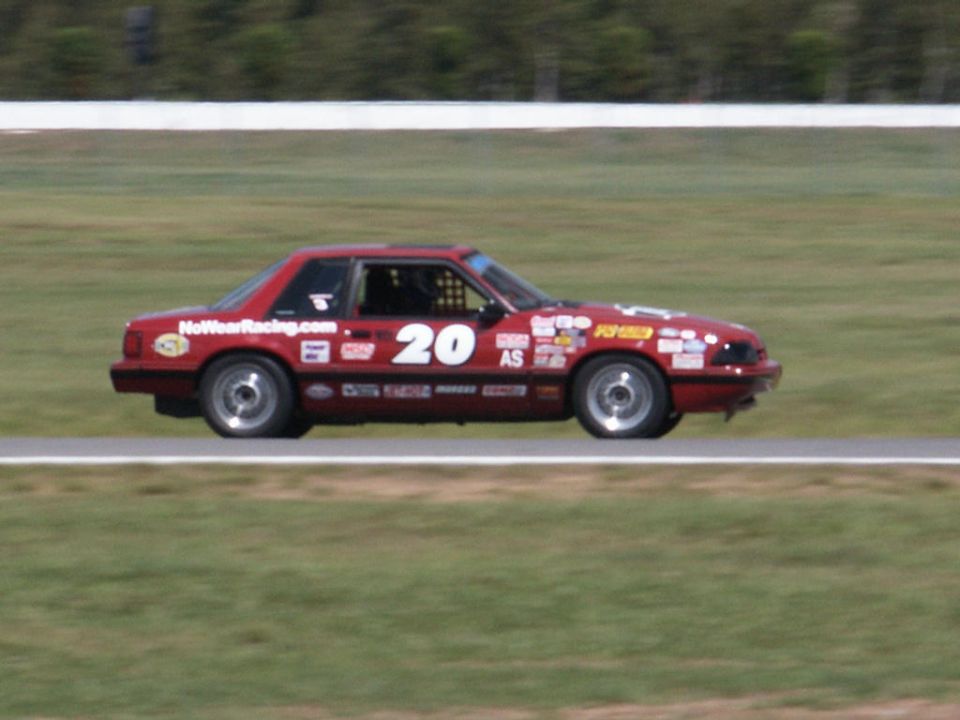 red race car with number 20 and various stickers on side, on track