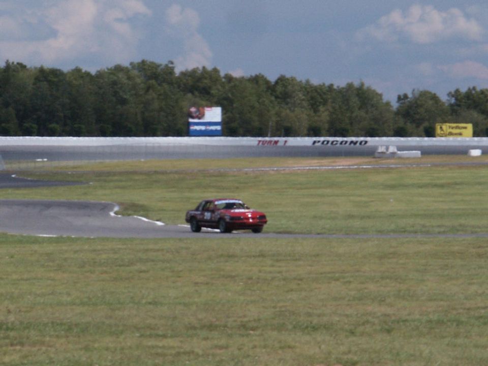 Red sedan on race track with 'TURN 1 POCONO' sign