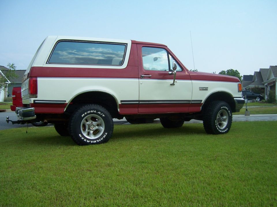 Red and white Ford Bronco parked on grass, side view