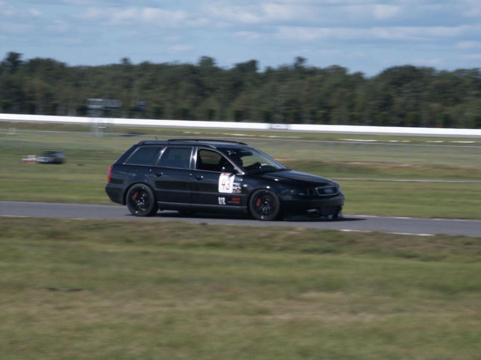 Black Audi wagon with racing numbers on door driving on a track