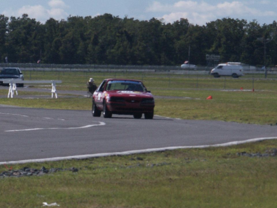 Red coupe on race track, another car and van in background