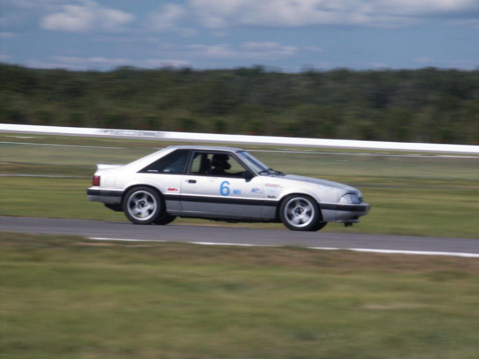 Silver coupe race car with blue number 6 on the door, driving on a track
