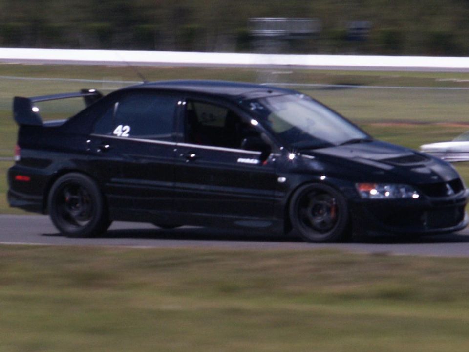 Black Mitsubishi Lancer Evolution VIII with racing number 42 on the door, seen from the front-right at a track