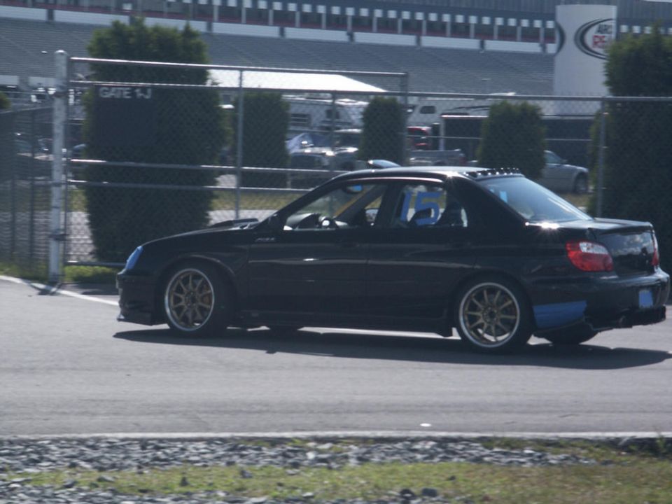 Black sedan with gold wheels and blue accents on rear bumper driving on a race track