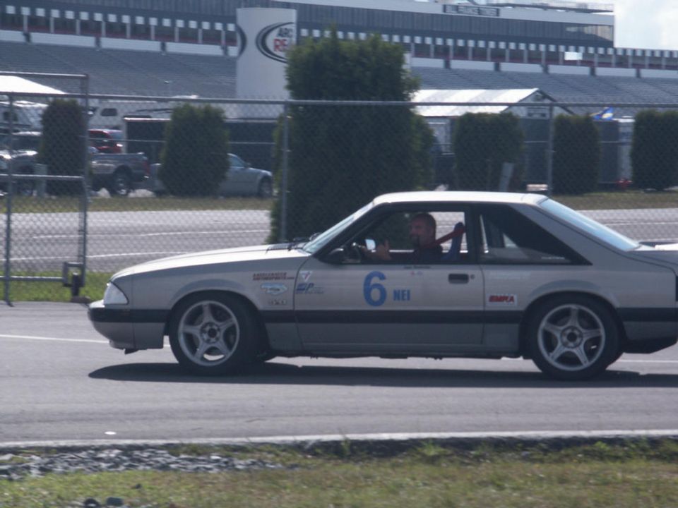 Silver race car with number 6 and 'NEI' on door, driving on a track