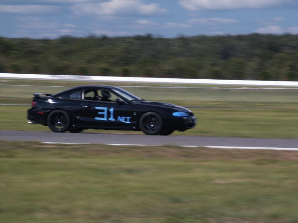 Black coupe with blue number 31.net on the door, driving on a race track