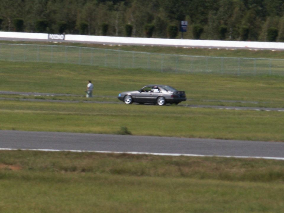 Gray 1987 Ford Mustang GT coupe on a racetrack, viewed from the right-front quarter angle