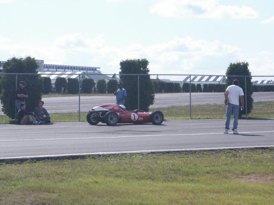 Red race car with white nose cone and number 1 on its side, parked on asphalt track