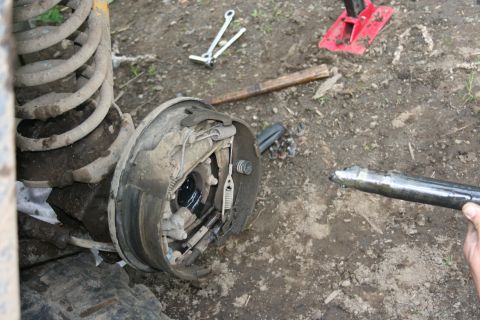 2004 Jeep TJ - A rear drum brake assembly and axle shaft are shown removed from a vehicle, with tools scattered on the ground.