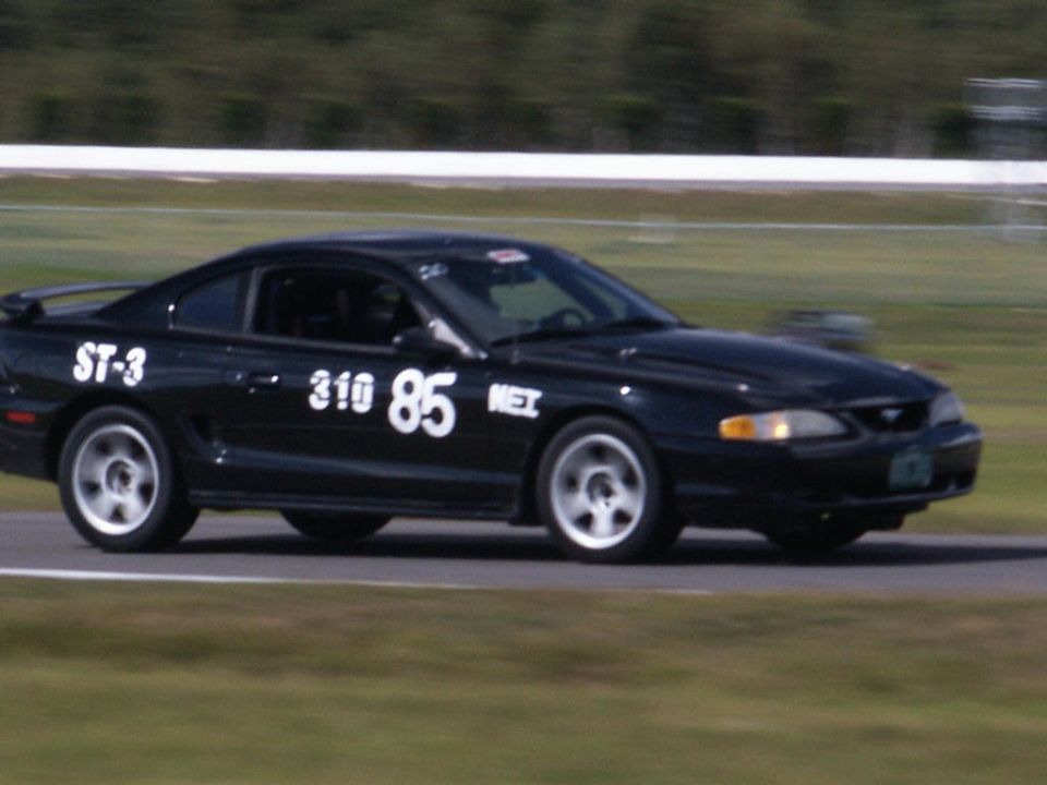 Black Ford Mustang race car with white numbers 310 85 and ST-3 on the side, driving on a track